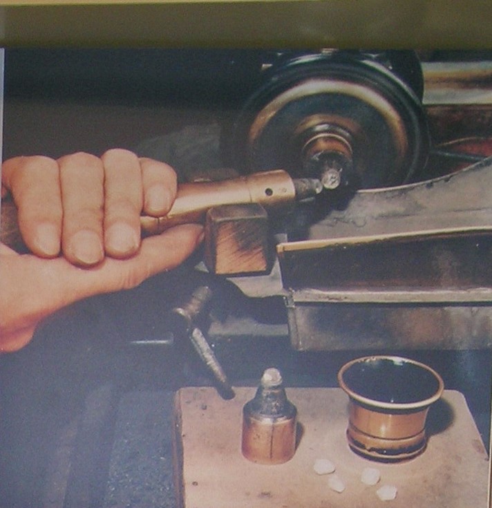 A hand of an artisan working on an old bruting machine. He is rubbing 2 rough diamonds together in order to shape them. This is a milestone in the history of diamond