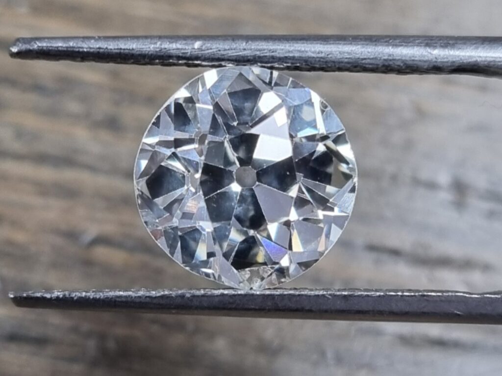 a 2 ct old european cut diamond being held in a tweezer on a wooden background