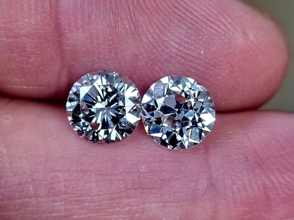 modern round diamond next to old european cut held between fingers