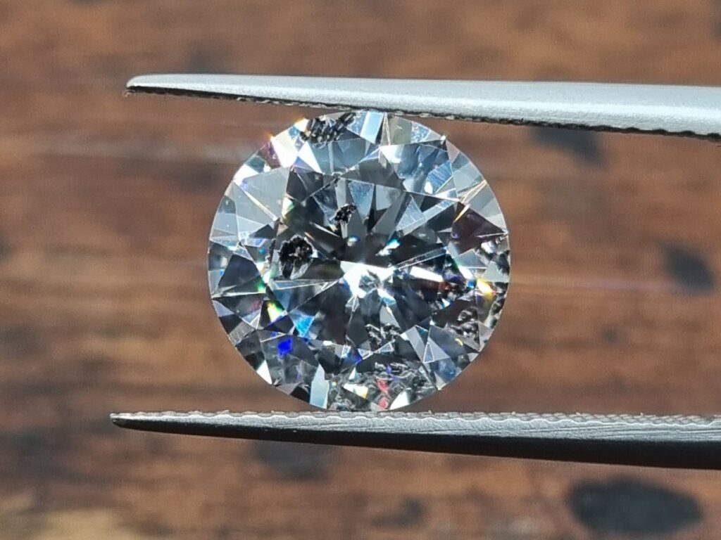 Round diamond held in tweezer on wooden background