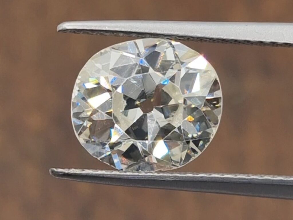 old mine cut diamond being held in a tweezer on a wooden background