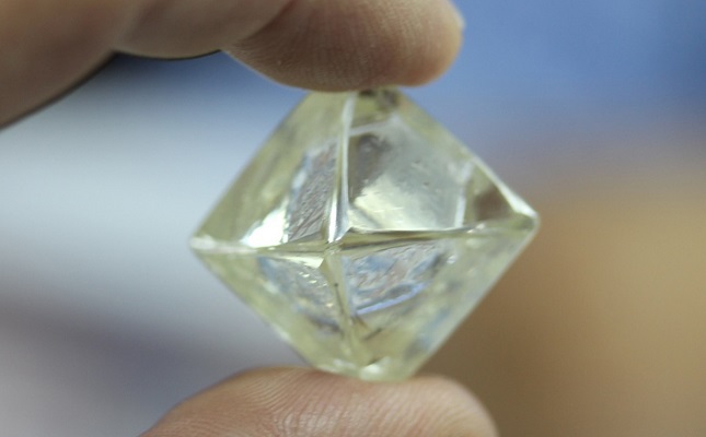 fingers holding an octahedral rough diamond crystal