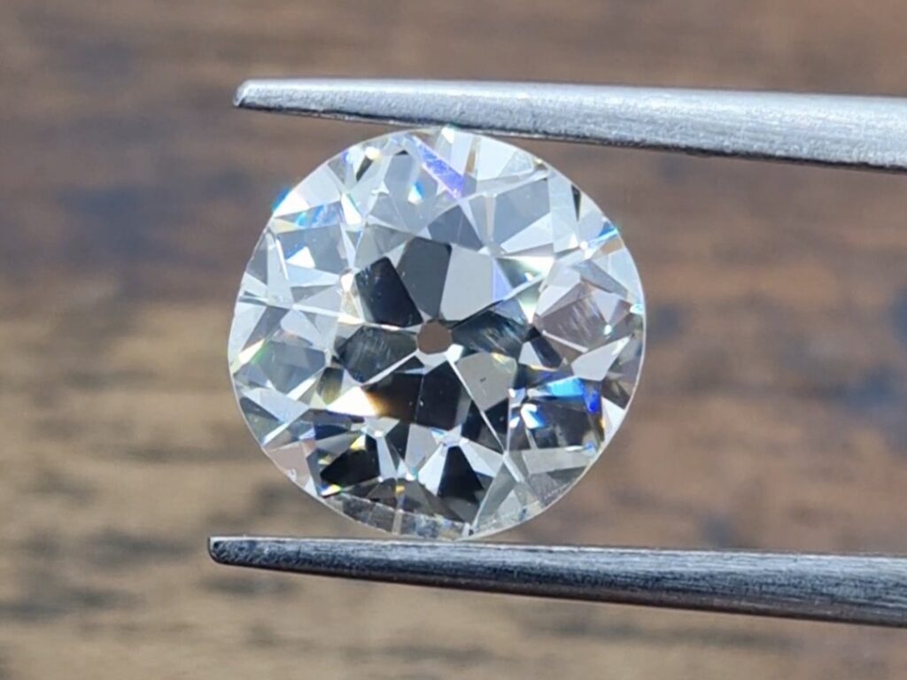 A 2 carat old european cut diamond held in a tweezer on a wooden background