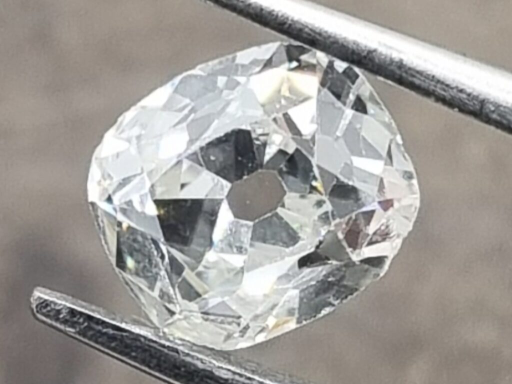 old mine cut diamond held in tweezer. gray background