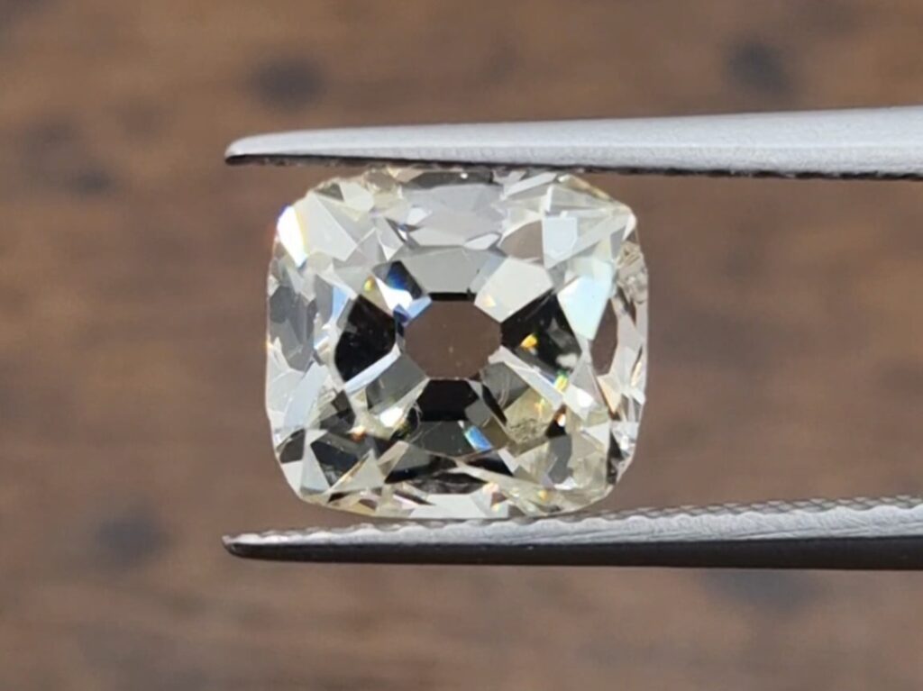 old mine cut diamond being held in a tweezer on a wooden background