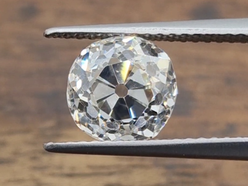 old mine cut diamond being held in a tweezer on a wooden background