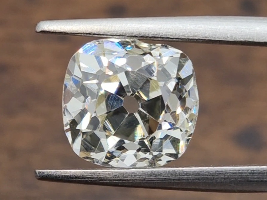 old mine cut diamond held in tweezer. brown background