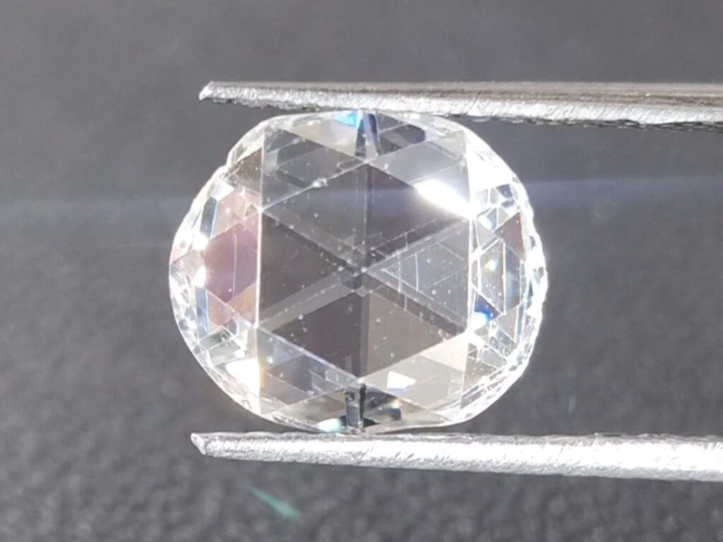 Antique rose cut diamond held in a tweezer on a gray background