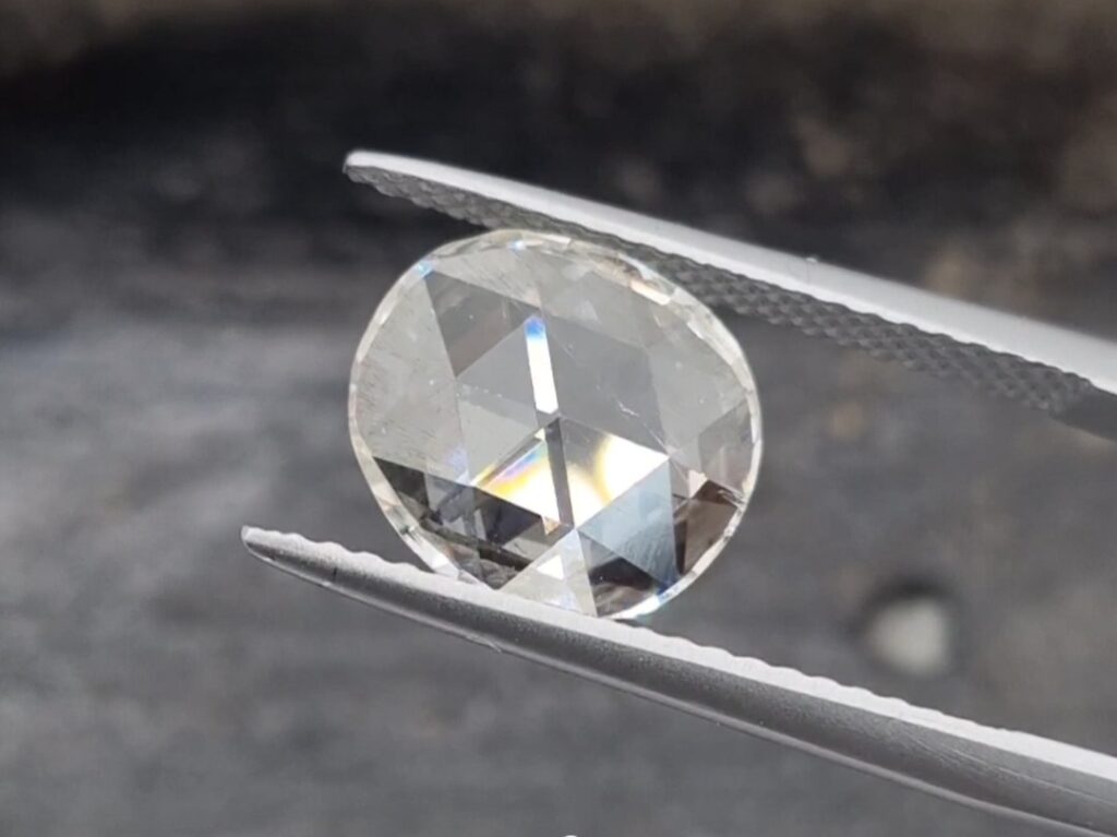 antique rose cut diamond held in a tweezer on a gray background