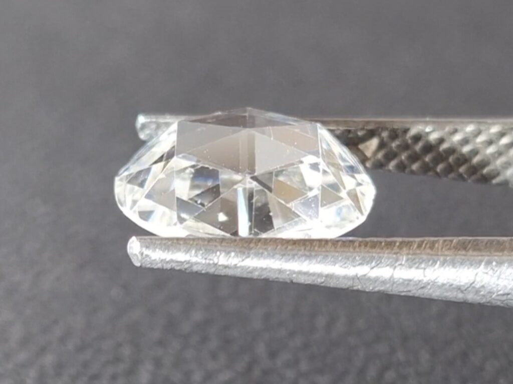 Antique rose cut diamond held in a tweezer on a gray background