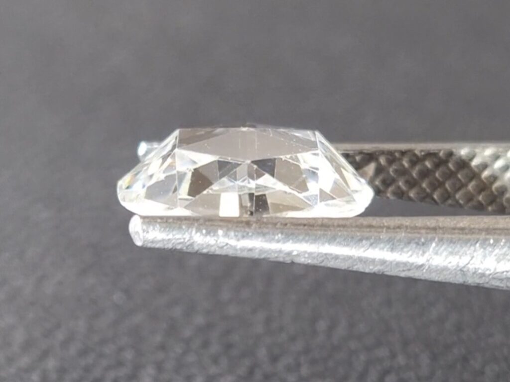 Antique rose cut diamond held in a tweezer on a gray background