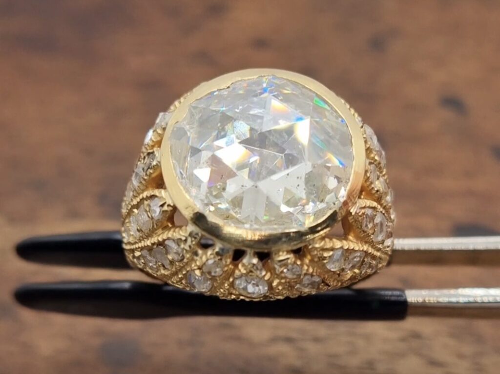 Antique ring with a rose cut diamond held in a tweezer on a wooden background