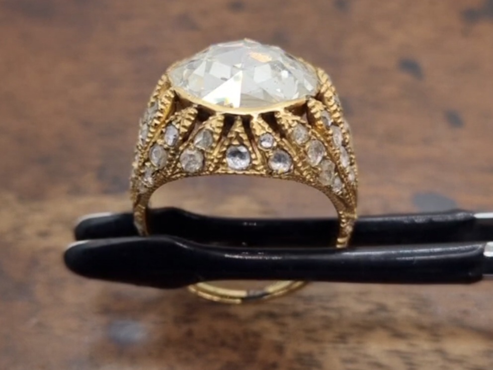 Antique ring with a rose cut diamond held in a tweezer on a wooden background