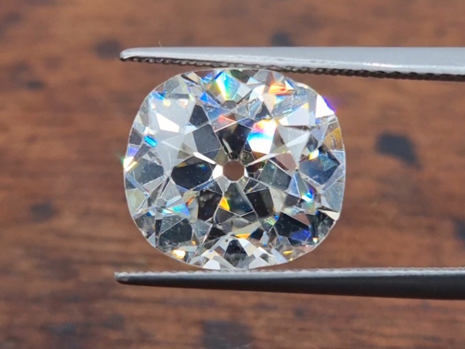 a 3ct old mine cut diamond held between tweezers on a wooden background